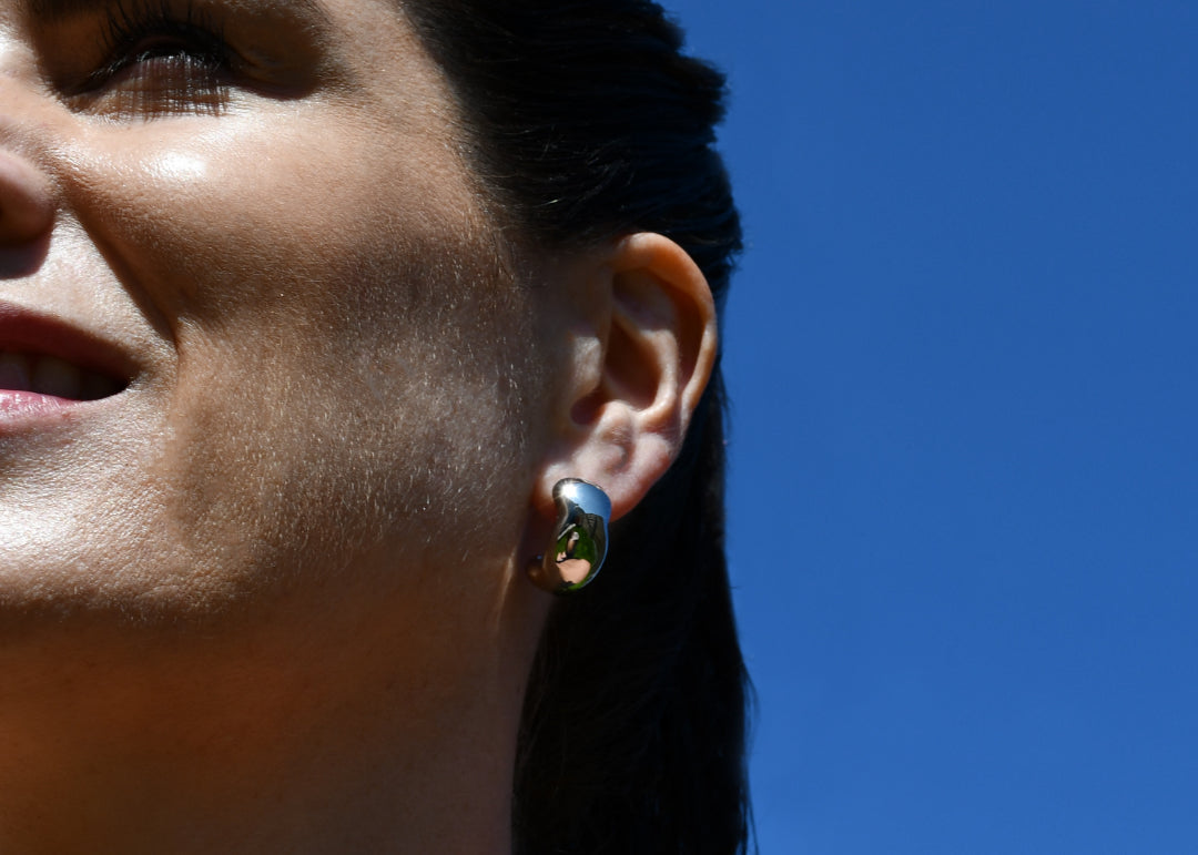 Woman Wearing Bold & imperfect chunky hoop silver earrings, dark hair, blue sky, tanned skin