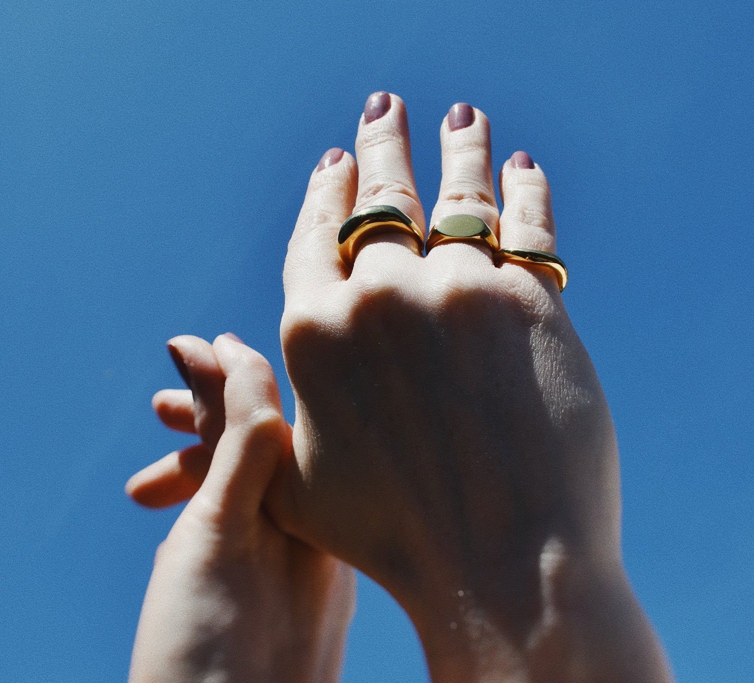 Raised hands wearing different rings and the Signature Signet Gold Ring. 