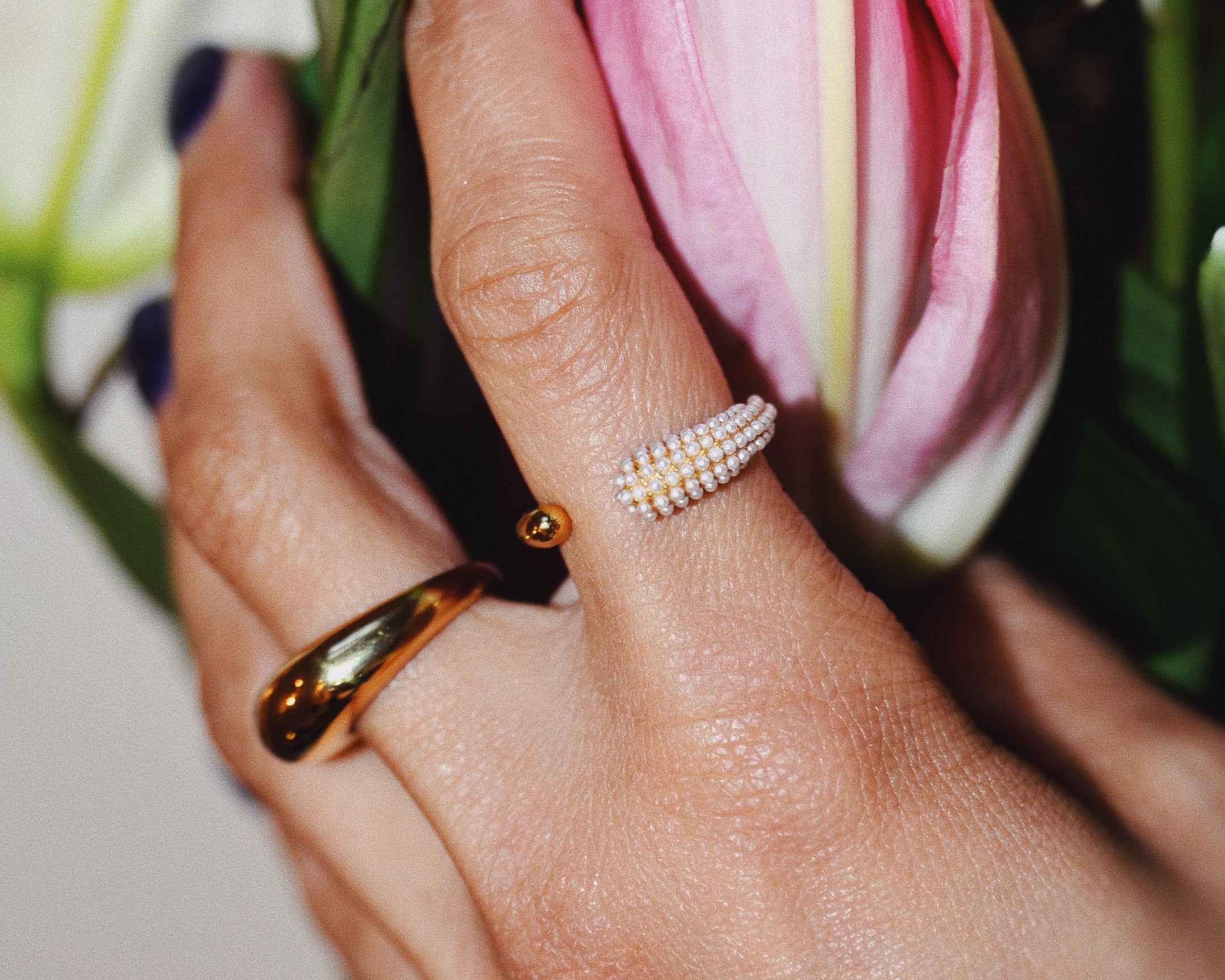 Hands holding pink flowers wearing the Sonia gold Ring and Pearl open front gold ring