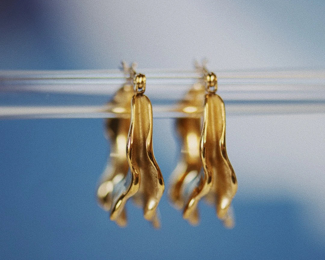 Fron view of the  Antonia Irregular Gold Hoop Earrings, with a blue background