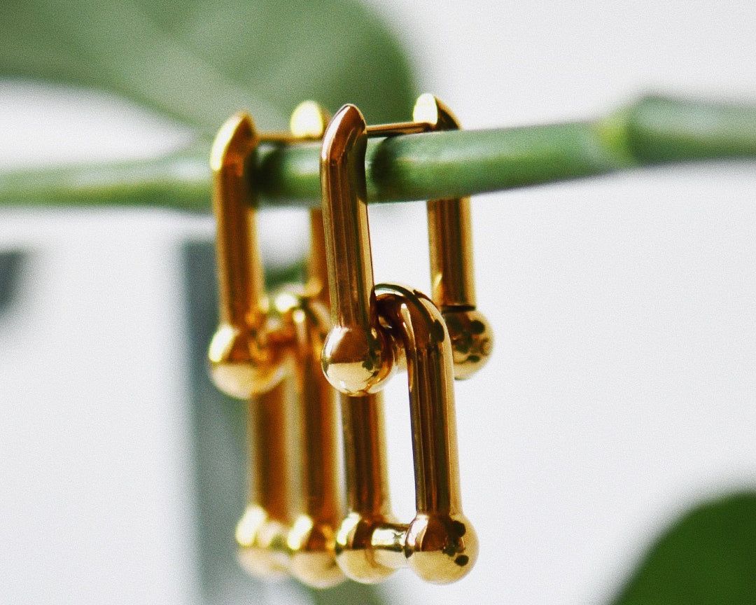 Seraphine Drop Gold Earrings hanging from a plant