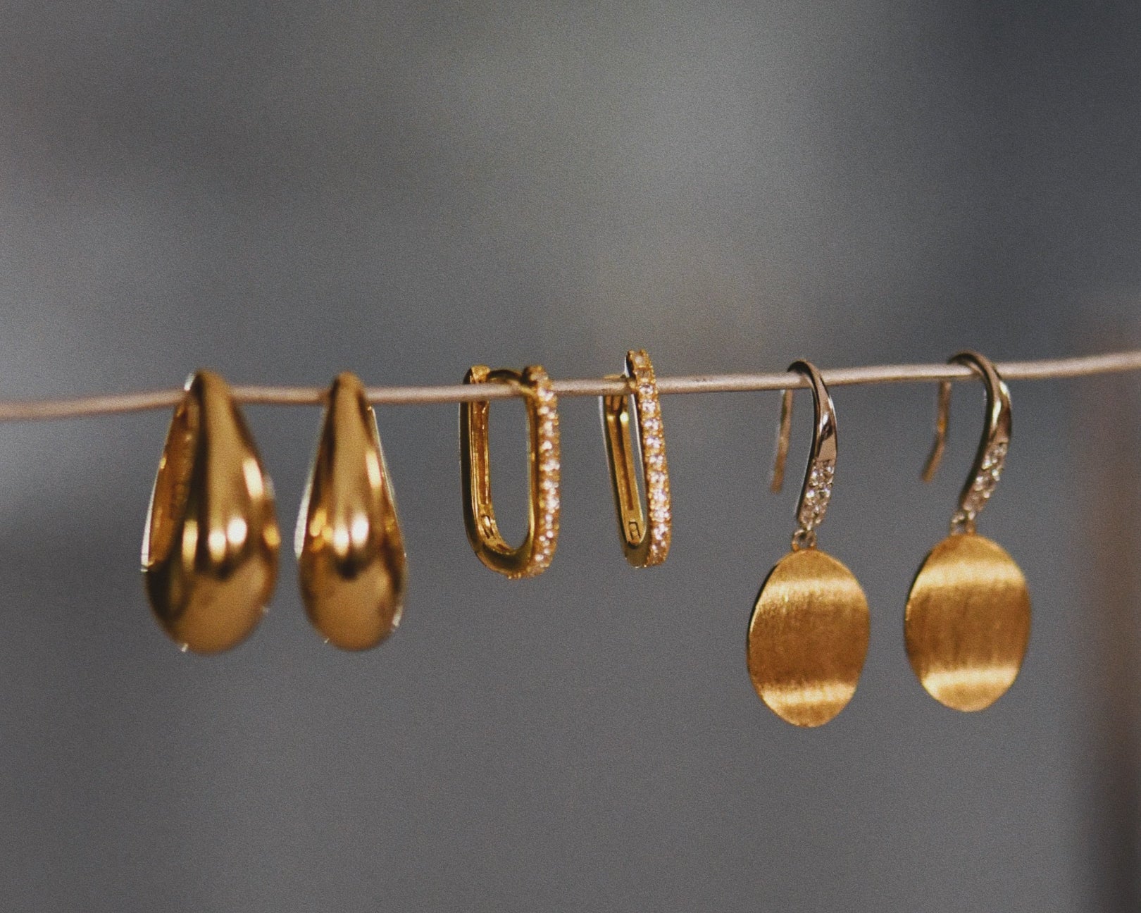 Three pairs of different earrings hanging on wire and the The Pavé Crystal Oval Hoops in the middle