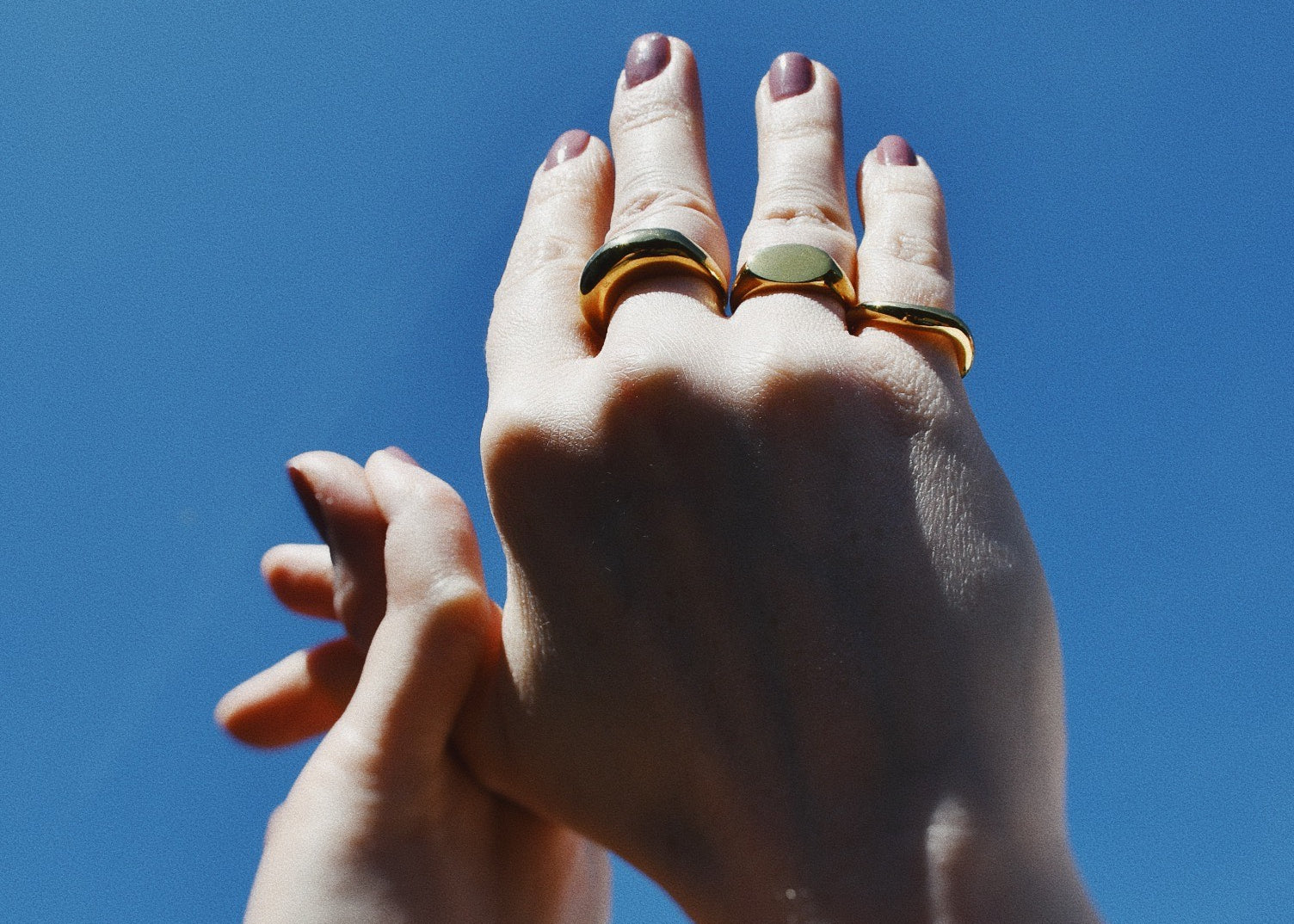 Raised hands wearing different rings and the Signature Signet Gold Ring. 